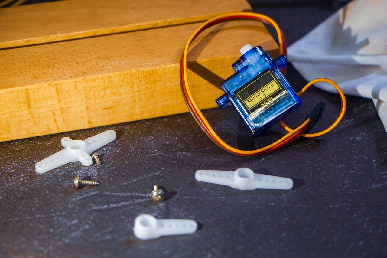Services Close-up of a micro servo motor with plastic arms and screws on a workbench, ideal for robotics projects.