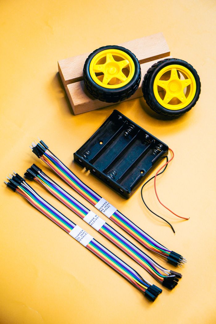 Services Robotics kit with wheels, wires, and battery holder on a yellow surface.