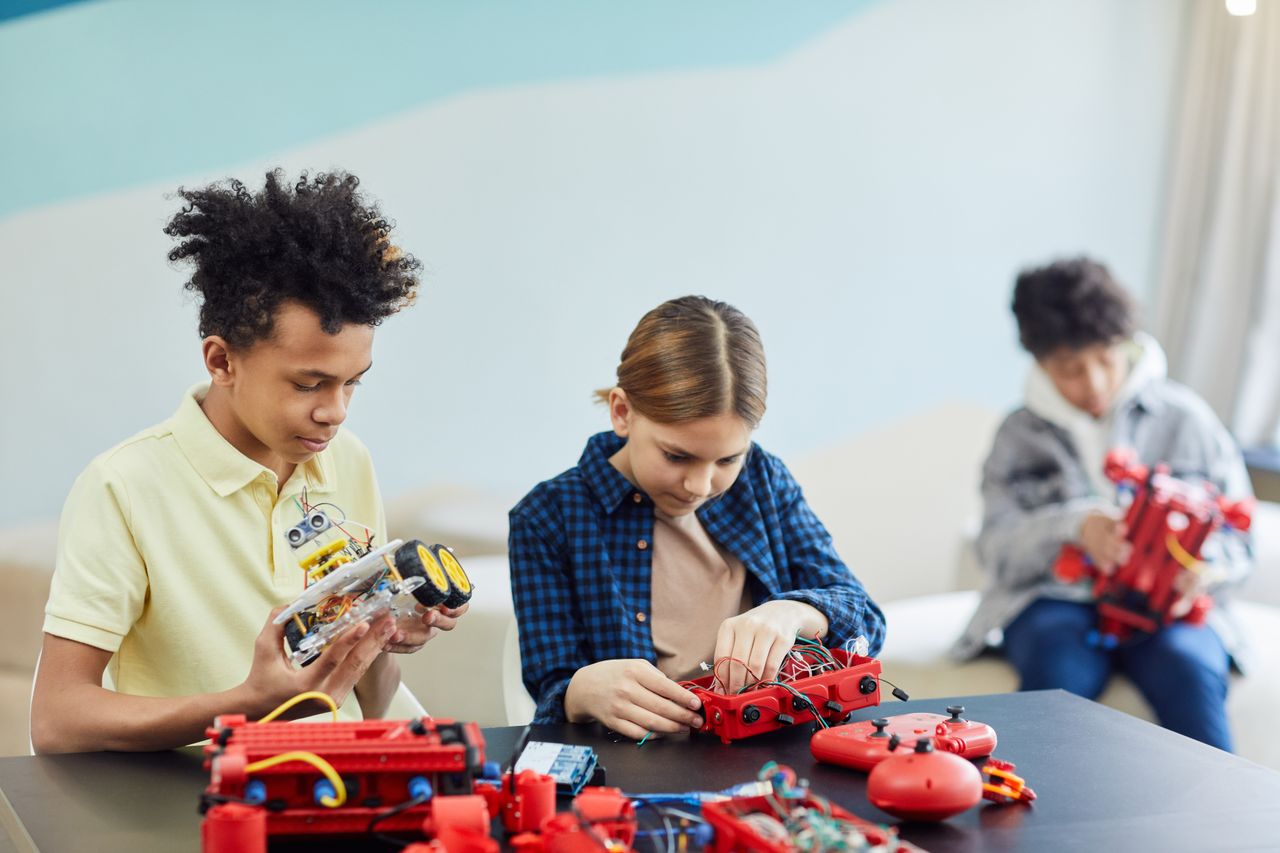 Services Three teenagers concentrating on robotics projects in a bright, indoor setting.