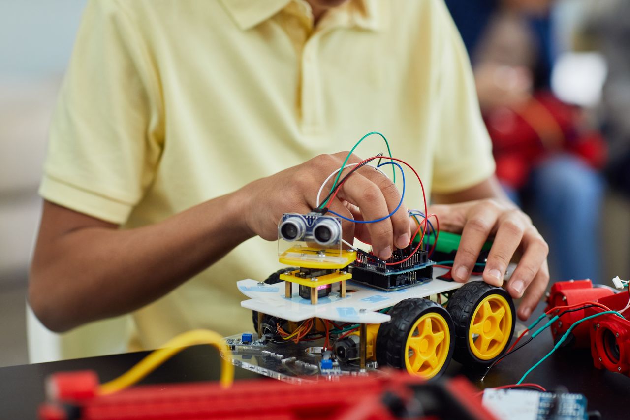 About A child engaging in a STEM activity by assembling a robotic toy car featuring electronics and wiring.