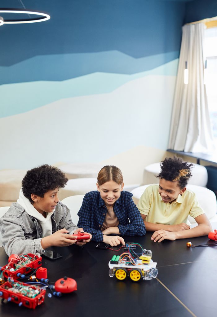 Services Three children building and playing with robotics at a table indoors.